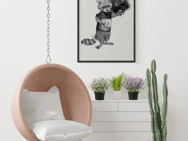 Un quadro con cornice nera che raffigura un procione antropomorfo con un libro in mano. Nell'ambiente dai colori chiari una cassettiera bianca con due piante sopra e una seduta sospesa con accanto un cactus.