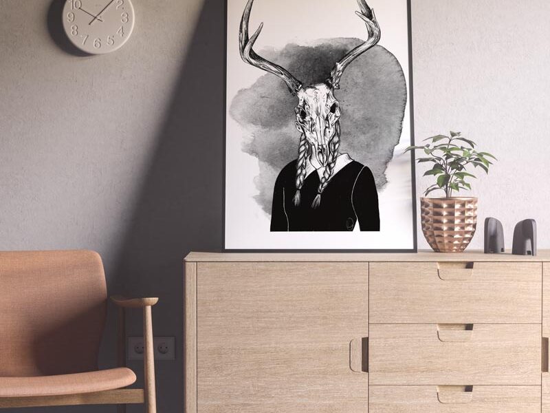 Su un mobile di legno chiaro è appoggiato un quadro con l’illustrazione di una donna con una maschera di osso di cervo.
